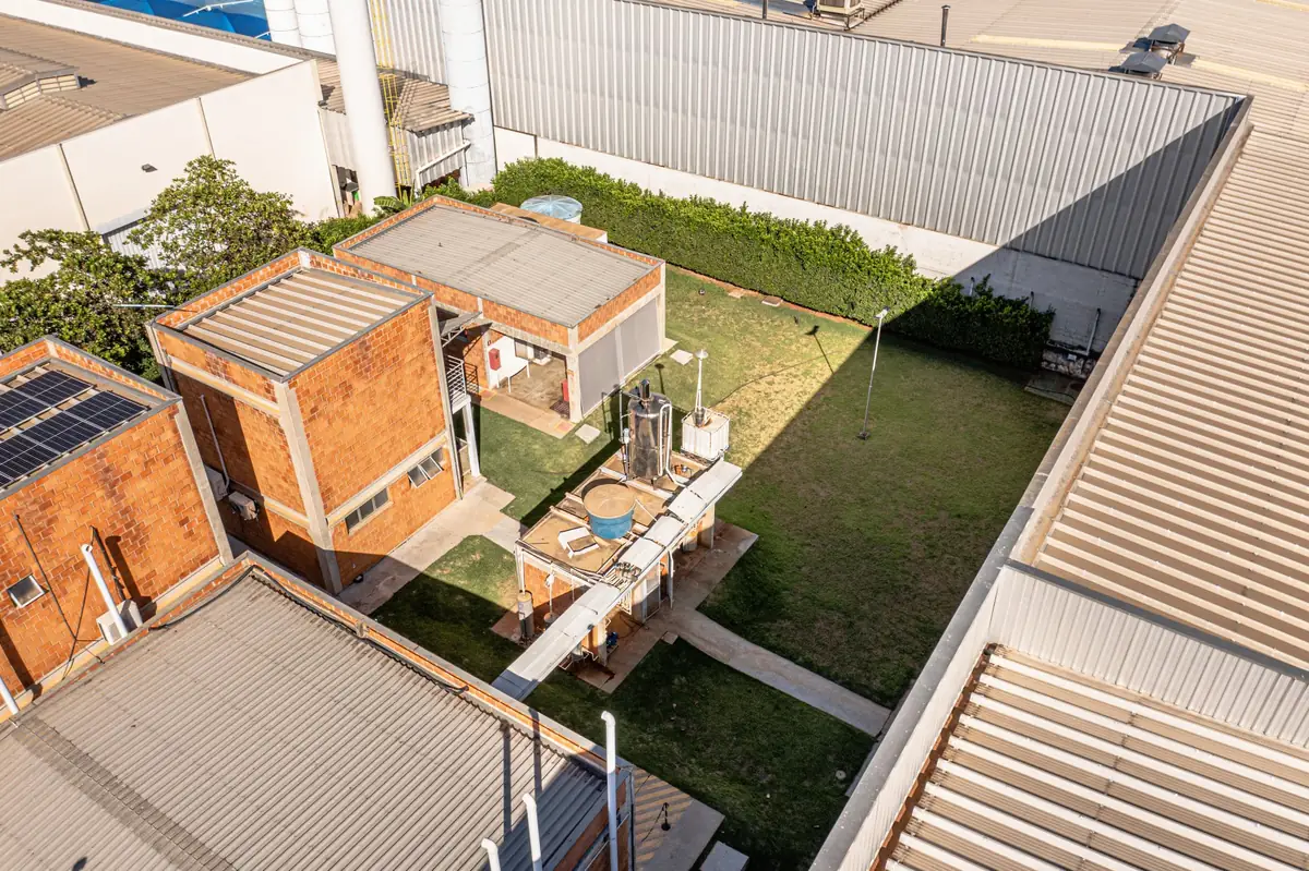 Vista aérea do pátio interno gramado da Oximed, entre os prédios de tijolos e galpões