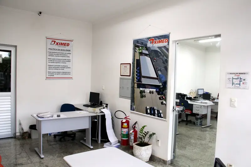 Sala administrativa da Oximed com mesa, computadores e o quadro da política da qualidade na parede