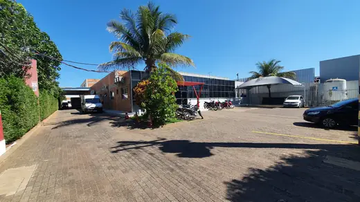Pátio de estacionamento da Oximed com coqueiro, veículos e os galpões ao fundo
